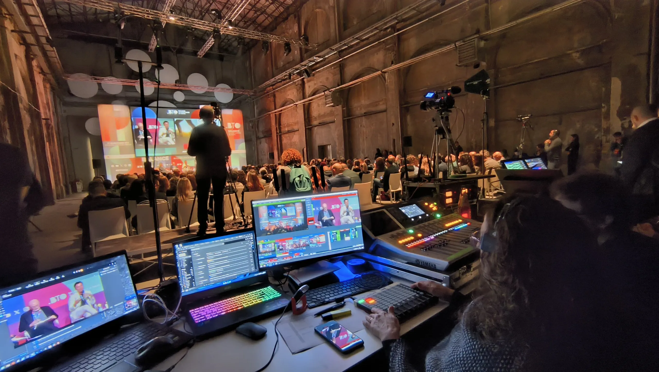 Regista che segue un convegno davanti al mixer video per la gestione di più camere e contributi